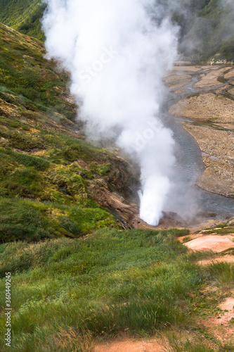 Daytime view in clear sunny weather of the valley of geysers. Mountains and volcanoes are visible on the horizon.