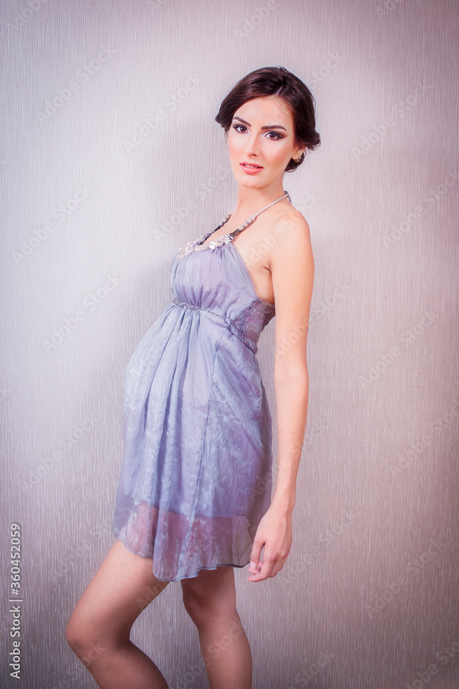 Fototapeta premium Sexy and Fit Pregnant Woman with Lavander Silk Dress, Standing in Profile, on Grey Background