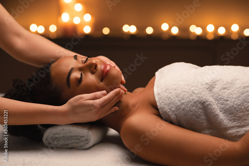 Relaxed african woman having face massage at spa