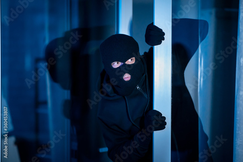 Burglar peeking into the house through an open glass door