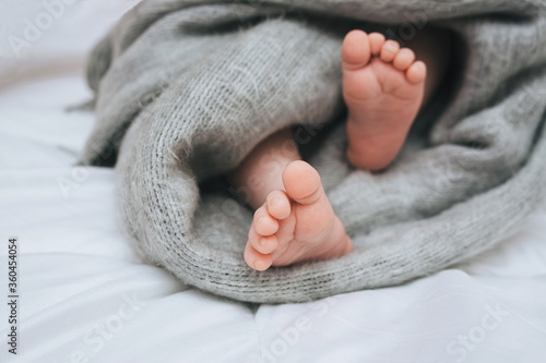 A small child sleeps on a white bed, covered with a gray plaid close-up. The legs of the newborn. Photography, concept.