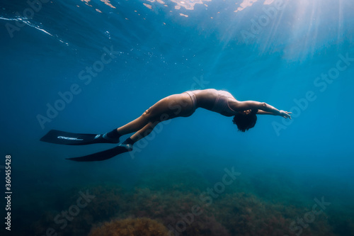 Sporty woman freediver with fins glides underwater in blue sea.