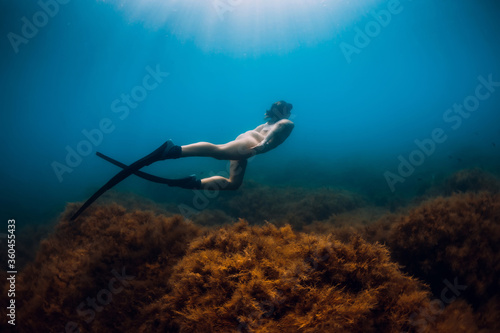 Sporty woman freediver with fins glides underwater in blue sea.