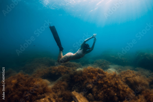 Sporty woman freediver with fins glides underwater in blue sea. © artifirsov