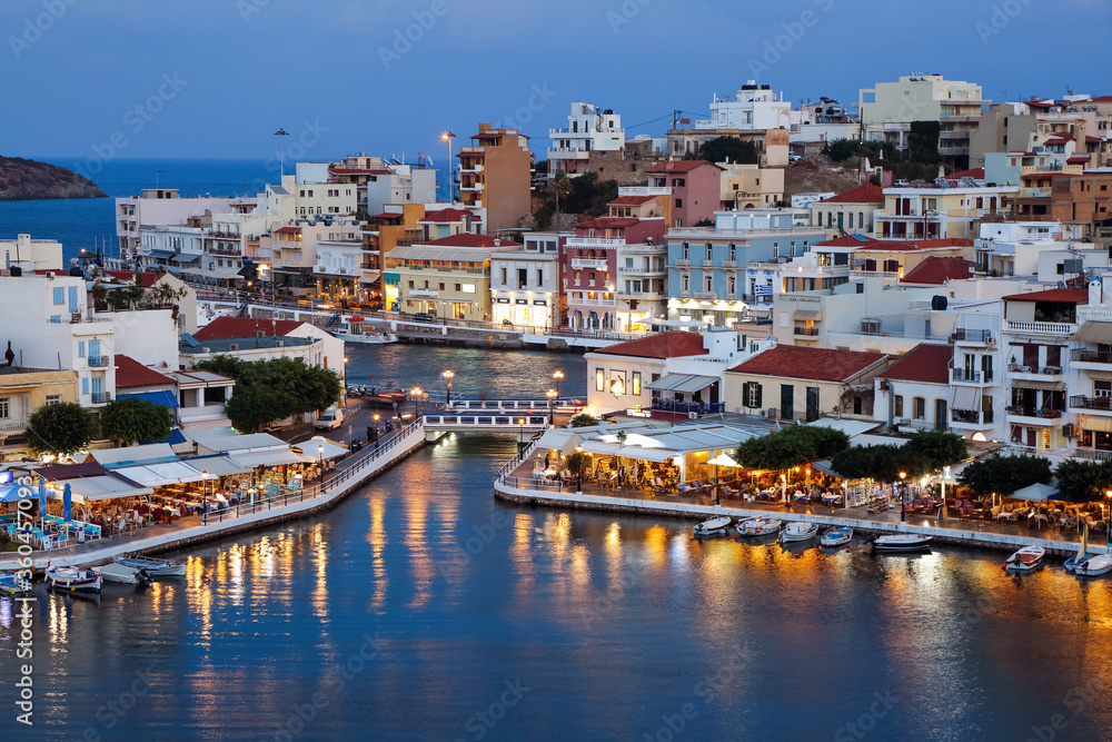 A panorama of the harbor city of Agios Nikolaos. View of the night sea, interesting landscapes, colorful houses, a coast view from the cafe. A popular tourist resort in the Greece.
