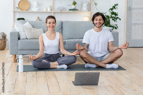 Healthy young couple meditating at home, looking at laptop screen