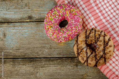 A pink and chockolate doughnut on a wooden planks background with a napkin on a vintage wood background with copy space.