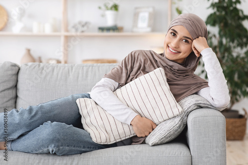 Home Relax. Smiling Arabic Girl In Headscarf Lying On Couch With Pillow