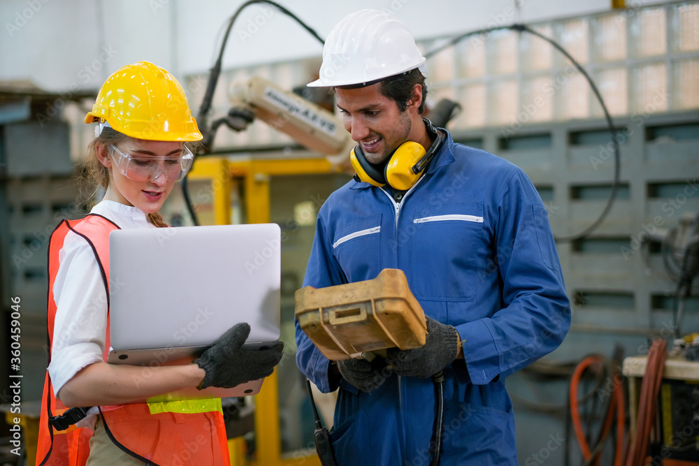 Factory worker man and woman with safety uniform discussion about robot working in factory workplace. They look happy with concept of good system and manager support for better industrial business. Factory worker man and woman with safety uniform discussion about robot working in factory workplace. They look happy with concept of good system and manager support for better industrial business.