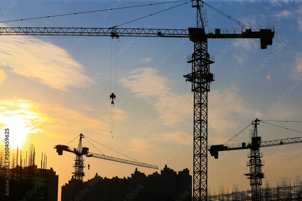 Cranes are silhouetted at a construction site at sunset