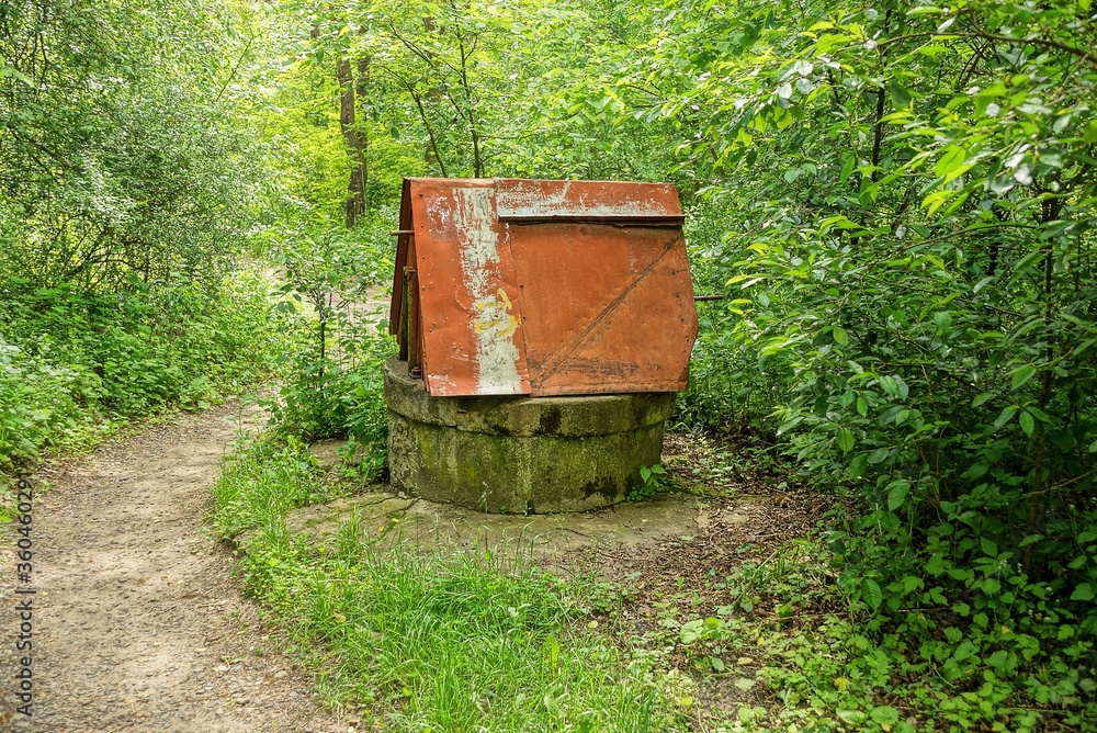 one old iron well in brown rust among green vegetation and trees in nature one old iron well in brown rust among green vegetation and trees in nature