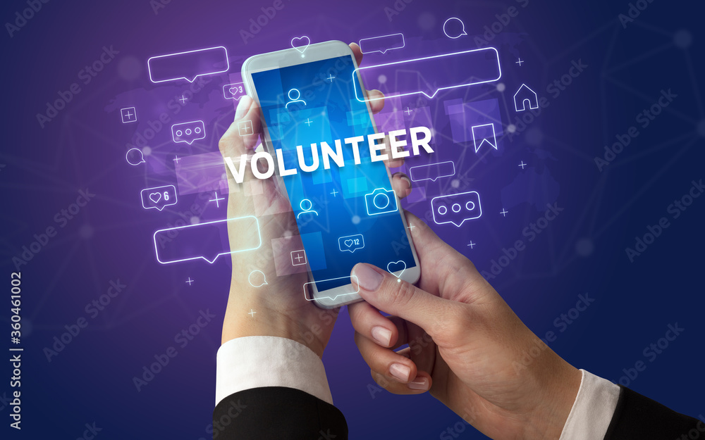 Female hand typing on smartphone with VOLUNTEER inscription, social media concept Female hand typing on smartphone with VOLUNTEER inscription, social media concept