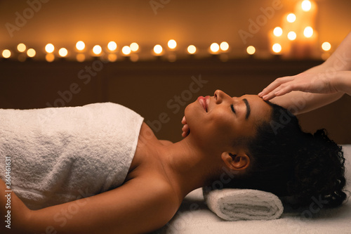 Relaxed black lady having face massage at spa