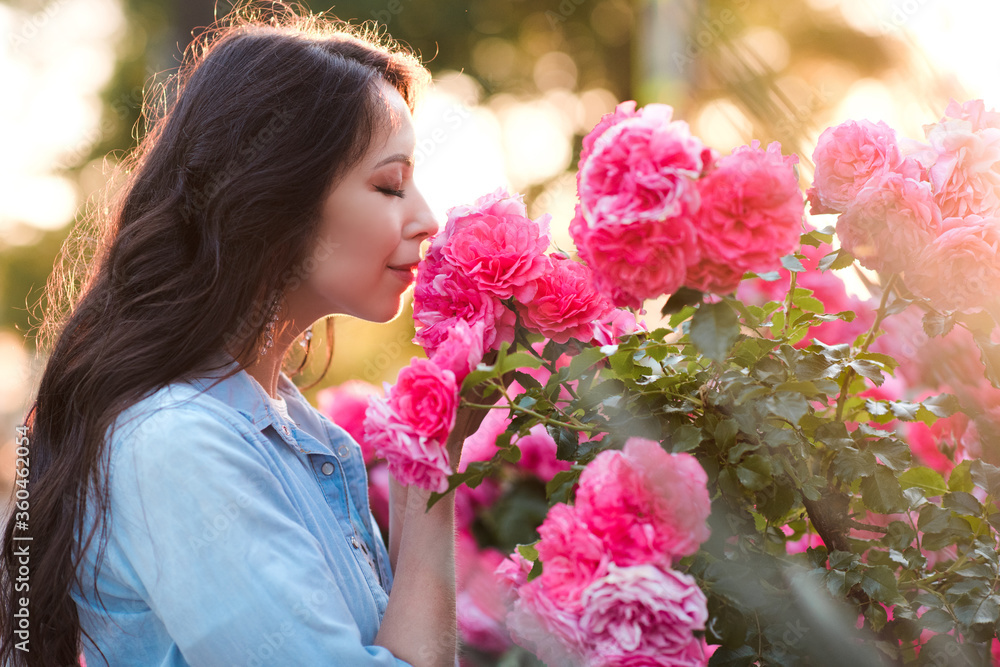 Fototapeta premium Beautiful woman 25-26 year old holding pink rose flowers in garden closeup. Summer season. 20s.