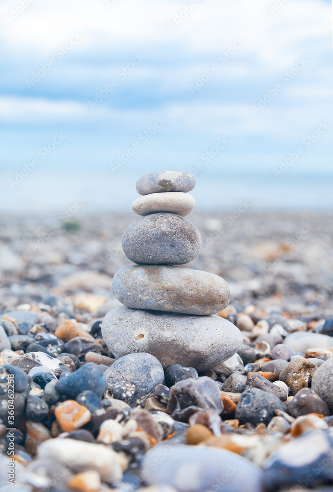 Grey pebble stones pyramid on the beach. Concept of zen, stability, harmony, balance. Close up, macro. front view. Blue ocean water on the background. North of France, Normandy Grey pebble stones pyramid on the beach. Concept of zen, stability, harmony, balance. Close up, macro. front view. Blue ocean water on the background. North of France, Normandy