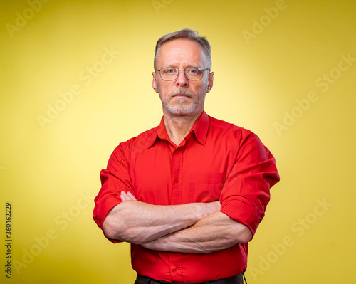 Half length picture of a mid aged business man smiling with arms crossed. solated on a yellow background © Vadim