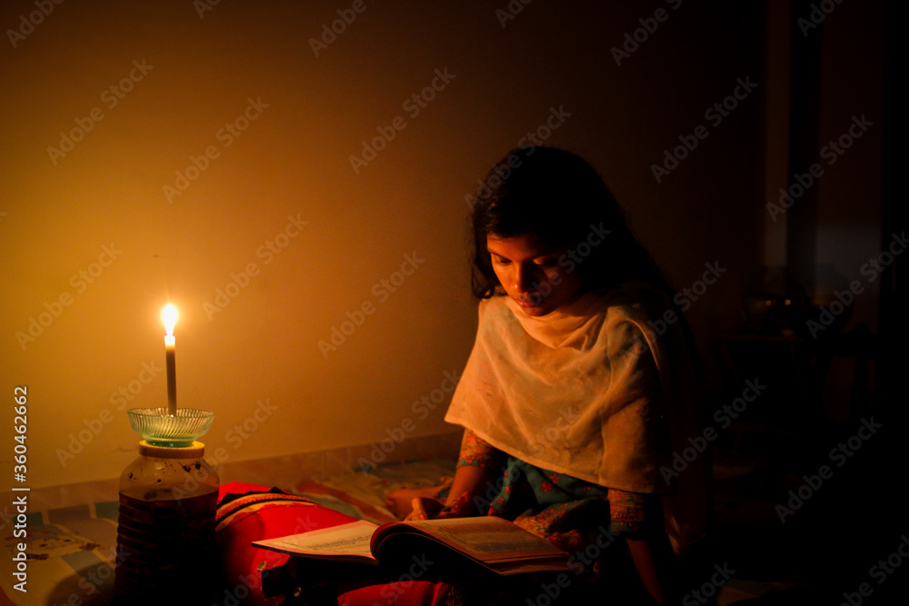 A young girl studying at home with candlelight after electricity load shedding at Dhaka City, Bnagladesh. Blackout. Electricity Problem. A young girl studying at home with candlelight after electricity load shedding at Dhaka City, Bnagladesh. Blackout. Electricity Problem.