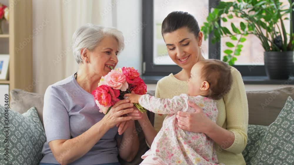 family, generation and celebration concept - mother with baby daughter giving grandmother flowers at home family, generation and celebration concept - mother with baby daughter giving grandmother flowers at home