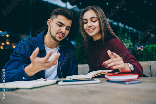 Funny hipster guy spending time with female colleague discussing ideas for project together, attractive woman student consulting with friend checking information from notepad on cafe terrace