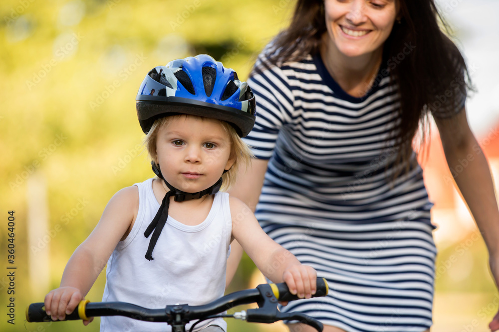 Fototapeta premium Young mother, helping her son to learn how to ride a bike, holding him and teaching him