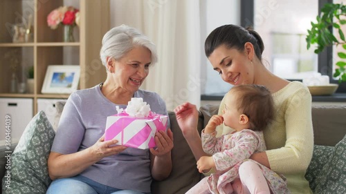 family, generation and greeting concept - mother with baby daughter giving gift box to grandmother at home
