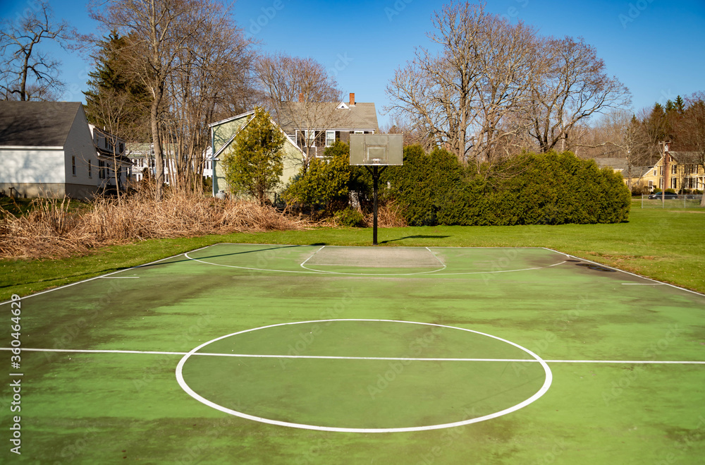 green recreational basketball court in a park with houses in background