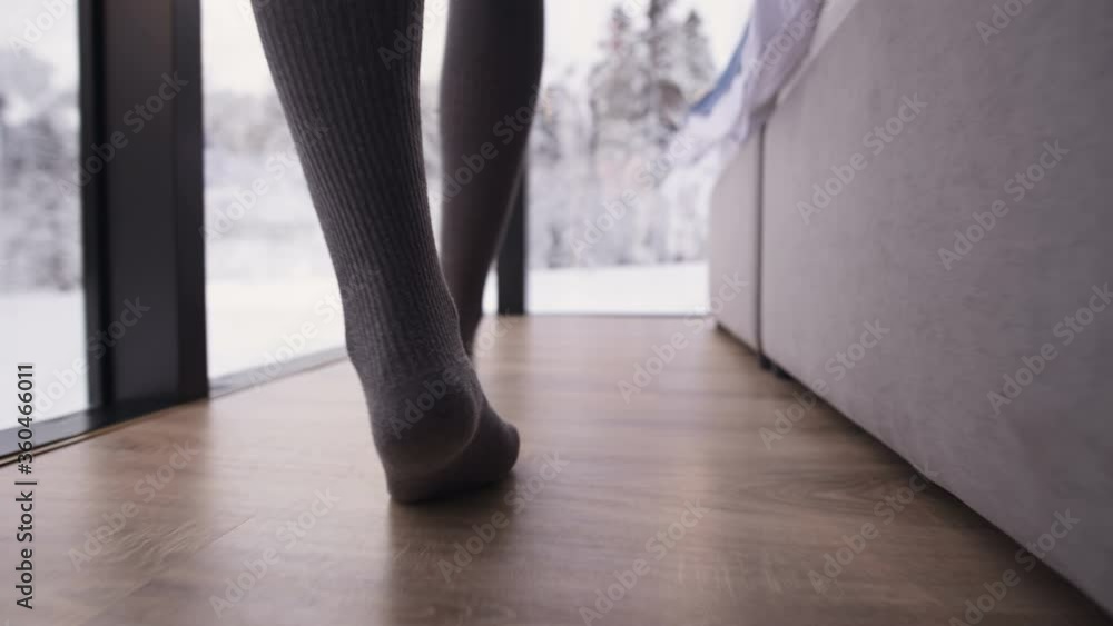 A close-up camera follows the feet of a girl in stockings walking on socks past a bed in a bedroom with transparent walled windows behind which winter forest and snow. A close-up camera follows the feet of a girl in stockings walking on socks past a bed in a bedroom with transparent walled windows behind which winter forest and snow.