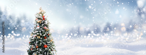 Beautiful Festive Christmas snowy background with holiday lights. Christmas tree decorated with red balls and knitted toys in forest in snowdrifts in snowfall on nature outdoors, panoramа, copy space. photo
