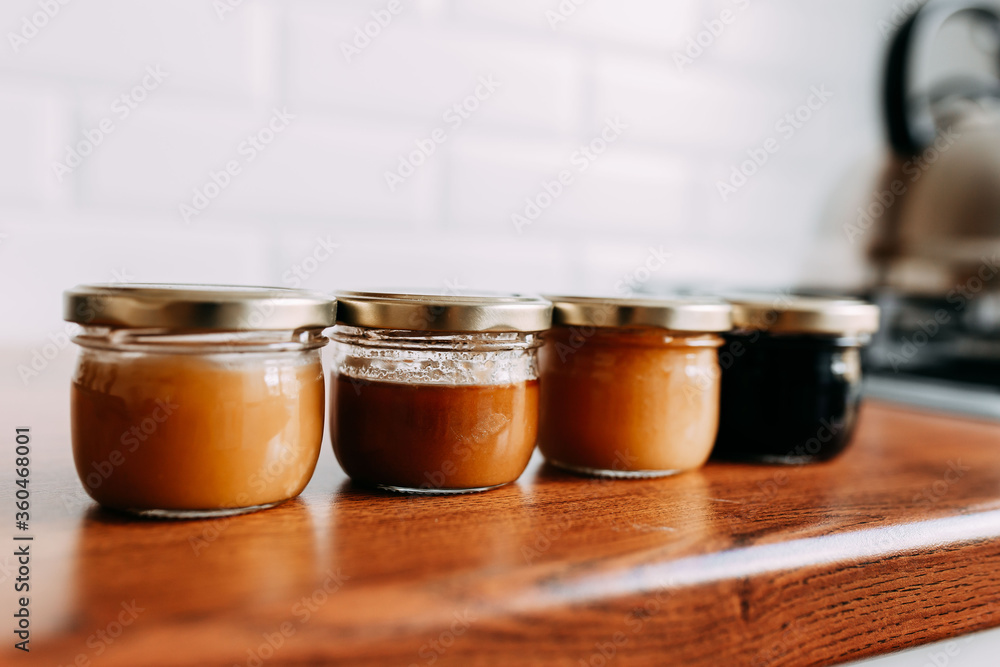 Little honey cans on the wooden table. Honey variety cans in a row. Bright kitchen interior. Wooden complete kitchen with gas oven Little honey cans on the wooden table. Honey variety cans in a row. Bright kitchen interior. Wooden complete kitchen with gas oven