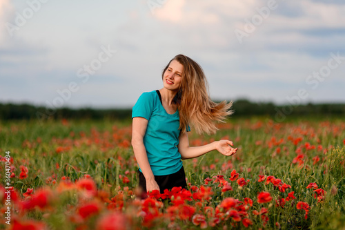 young smiling woman with long hair standing on field with red poppies.
