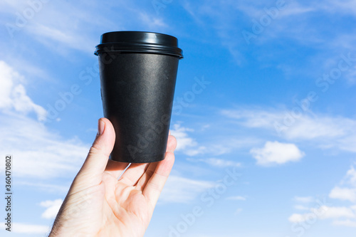 Holding a black paper cup in the background of blue sky