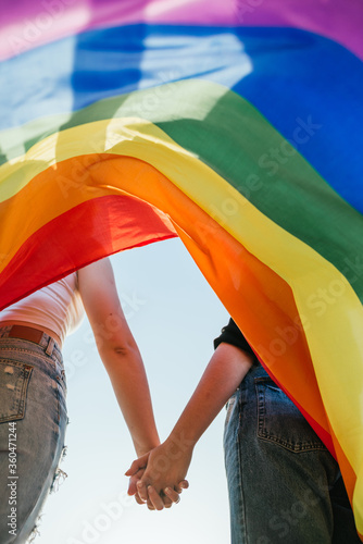 Fotografie two girls hold hands at sunset with a rainbow flag of LGBT pride