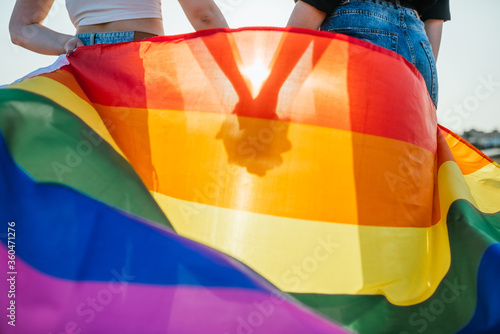 silhouette of two girls holding hands at sunset with a rainbow flag of LGBT gay pride. photo