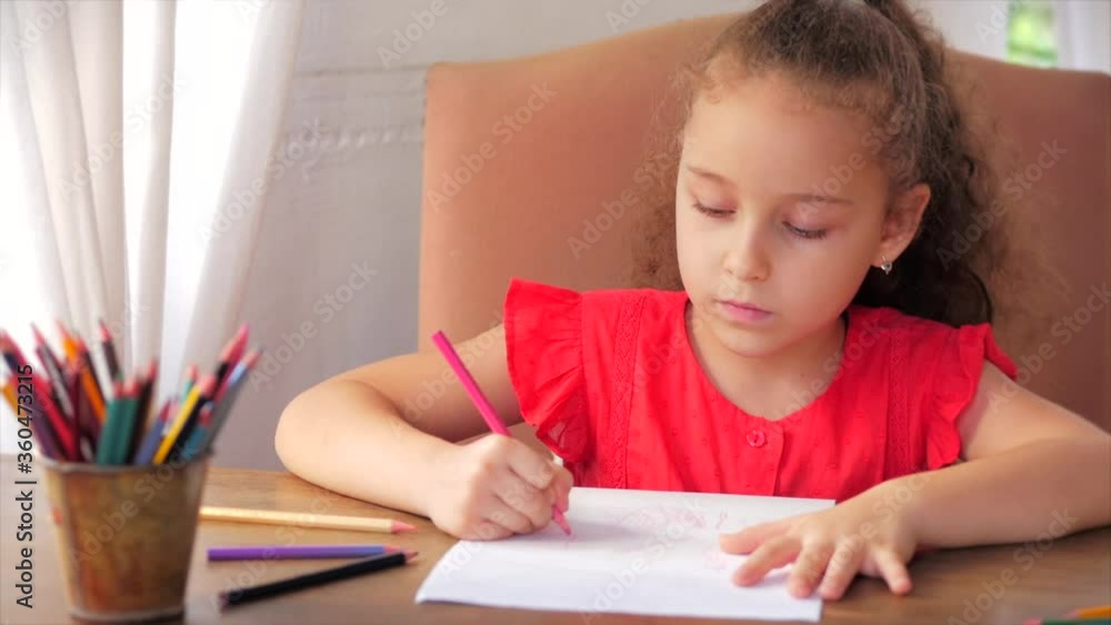 Happy Little Girl or Cute primary child school child of 7-8 years old at home relaxing sits in house and paints on paper use colour pencils. Child draws,focused children elementary education concept. Happy Little Girl or Cute primary child school child of 7-8 years old at home relaxing sits in house and paints on paper use colour pencils. Child draws,focused children elementary education concept.