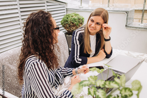 Two young beautiful smiling girl office workers discuss an important successful business project in a free environment in a cafe