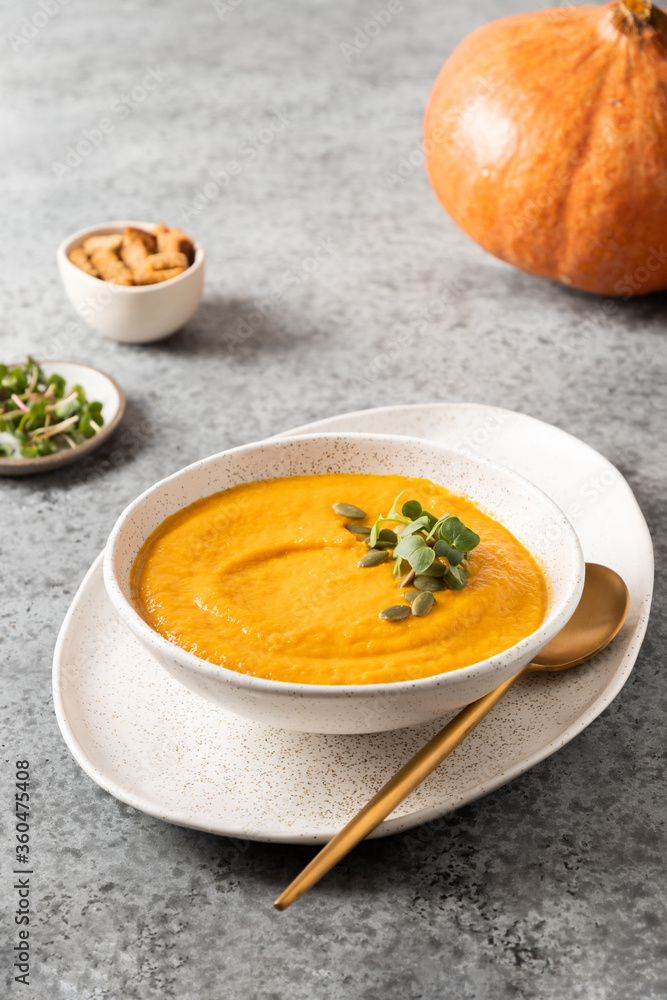 Pumpkin soup with cream garnish microgreens on grey background. Vertical format. Close up. Pumpkin soup with cream garnish microgreens on grey background. Vertical format. Close up.