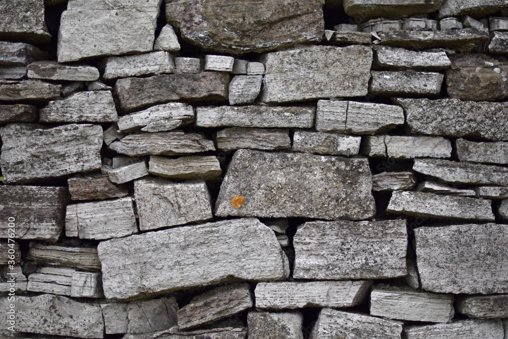 Obraz premium Background of dry stone wall at Monsal Dale in the Peak District National Park. Angular stones with visible sediments. Xanthoria lichen both yellow and sun bleached on the surface.