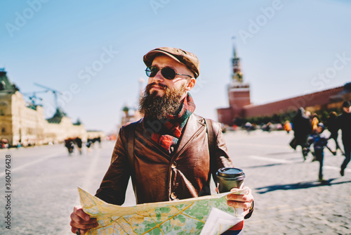 Canvas Print Good looking male tourist in leather cap and jacket looking on building during s