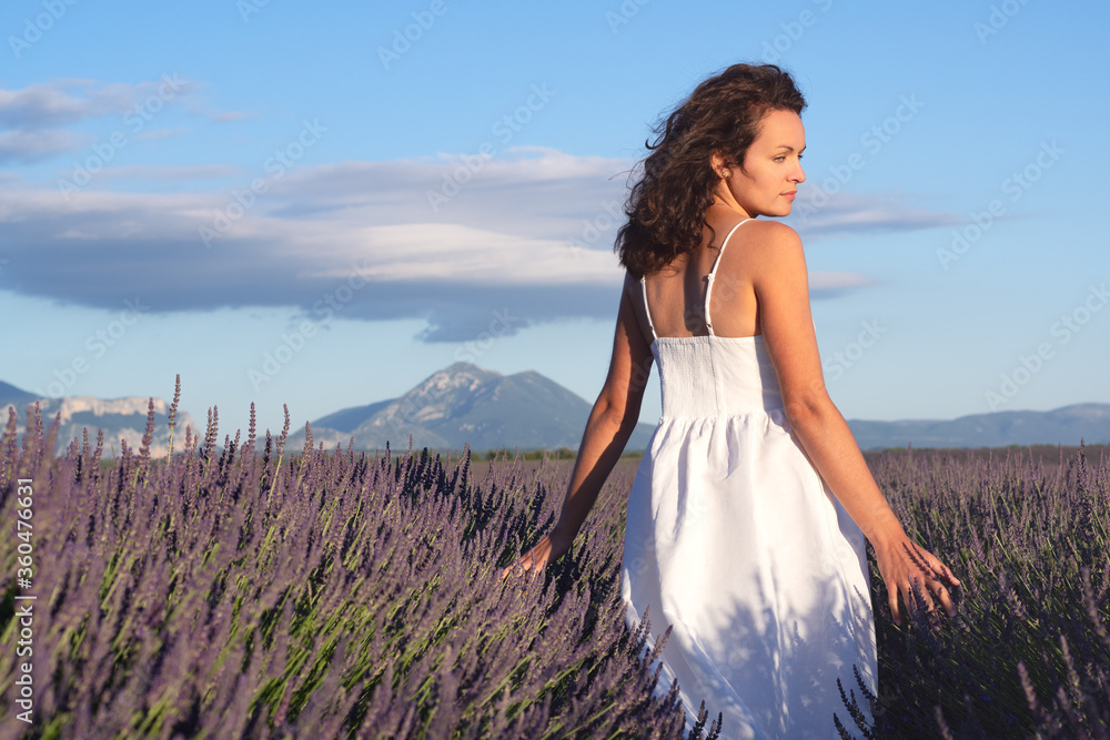 Obraz premium Summertime in lavender. Young beautiful woman in lavender flowers field at sunset in white dress. Provence. France.