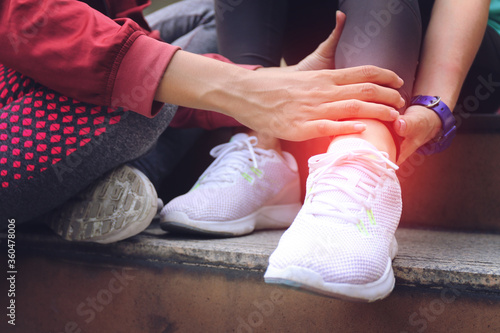 Athletic woman runner touching foot in pain due to sprained ankl