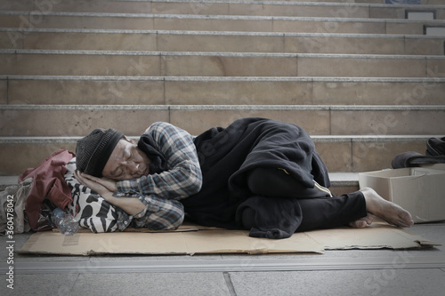Homeless man sleeps on the street in the shadow of the building