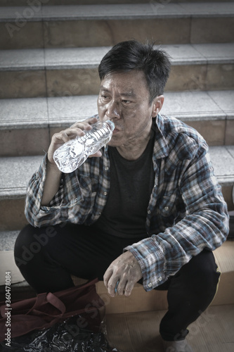 poor homeless young man sitting drinking water from a plastic bo