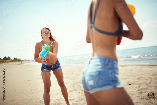 Two sexy girl with water guns have fun on the beach by the sea.