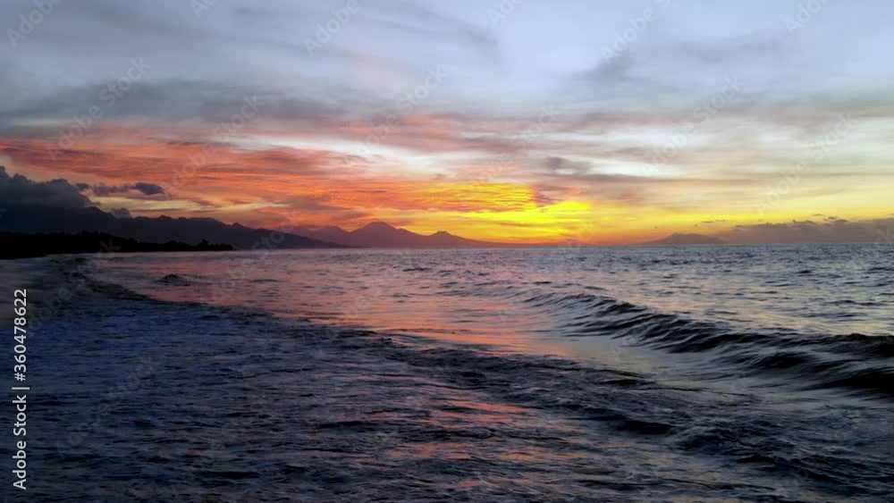 Relaxing sunset in Bali while waves roll onto the beach with mountains glowing in the distance. Relaxing sunset in Bali while waves roll onto the beach with mountains glowing in the distance.