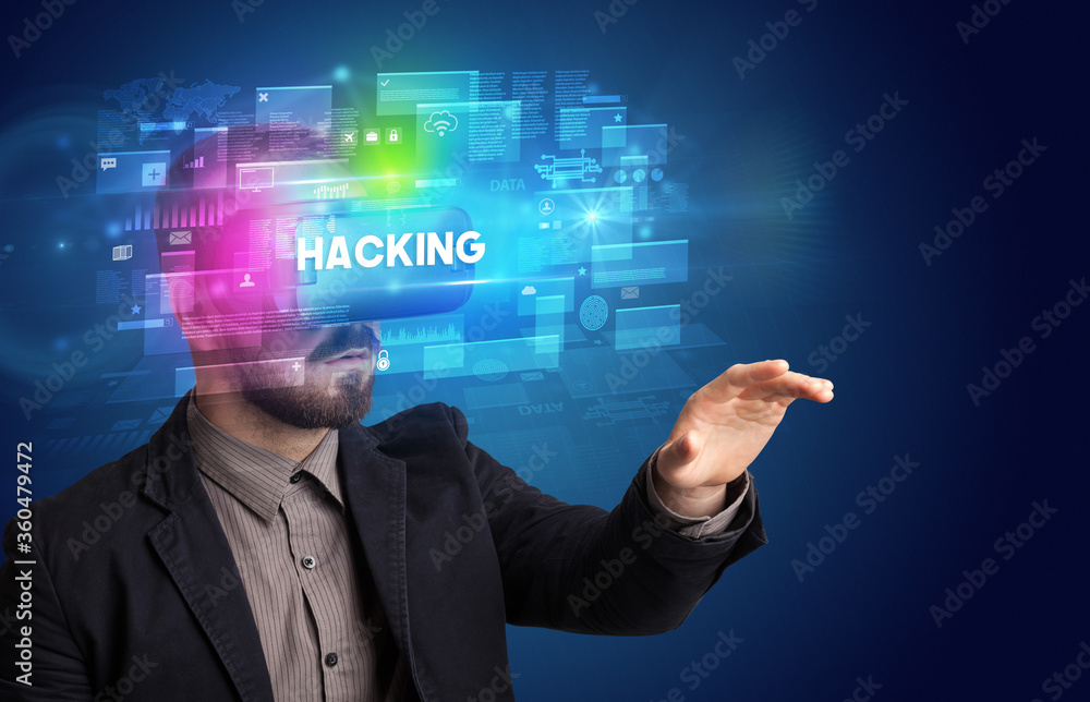 Businessman looking through Virtual Reality glasses with HACKING inscription, innovative security concept Businessman looking through Virtual Reality glasses with HACKING inscription, innovative security concept
