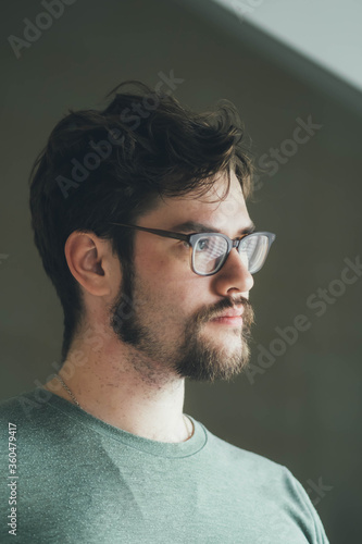 a handsome young man with a thick beard and glasses is illuminated on one side by a soft light. fashionable beard, happy. reflection in the mirror. irritation after shaving. shaves three times