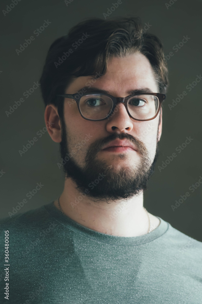 a handsome young man with a thick beard and glasses is illuminated on one side by a soft light. fashionable beard, happy. reflection in the mirror a handsome young man with a thick beard and glasses is illuminated on one side by a soft light. fashionable beard, happy. reflection in the mirror