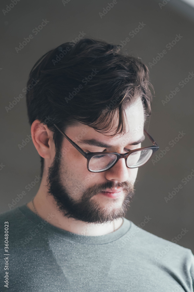 a handsome young man with a thick beard and glasses is illuminated on one side by a soft light. fashionable beard, happy. reflection in the mirror a handsome young man with a thick beard and glasses is illuminated on one side by a soft light. fashionable beard, happy. reflection in the mirror