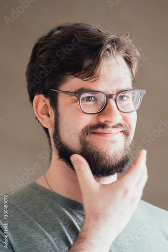 a handsome young man with a thick beard and glasses is illuminated on one side by a soft light. fashionable beard, satisfied