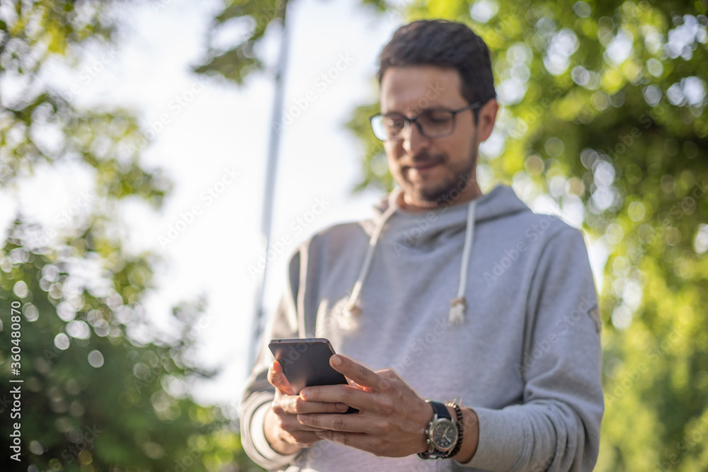 Smart looking man texting message on smartphone in park, back light Smart looking man texting message on smartphone in park, back light